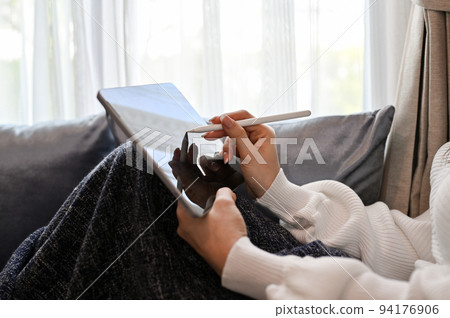 Close-up image, A female relaxes in the living room, sits on sofa and uses a digital tablet. Close-up image, A female relaxes in the living room, sits on sofa and uses a digital tablet. 94176906