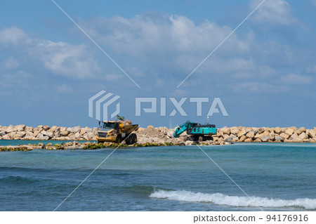 An excavator and a mining truck move stones into the sea. Construction of breakwaters to protect the beach in Netanya in Israel. An excavator and a mining truck move stones into the sea. Construction of breakwaters to protect the beach in Netanya in Israel. 94176916