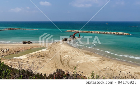 An excavator and a mining truck move stones into the sea. Construction of breakwaters to protect the beach in Netanya in Israel. An excavator and a mining truck move stones into the sea. Construction of breakwaters to protect the beach in Netanya in Israel. 94176923