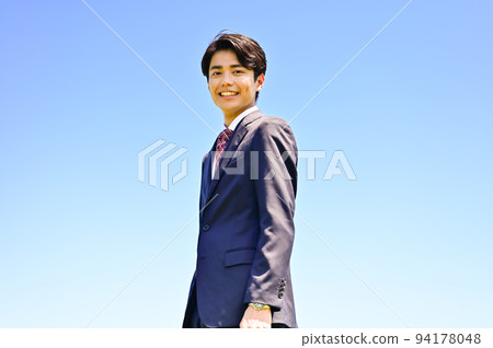 Young businessman with blue sky background Young businessman with blue sky background 94178048