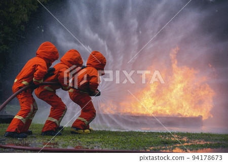 Firefighter Rescue team training in fire fighting extinguisher. Firefighter teamwork fighting with flame using fire hose chemical water foam spray engine. Fireman wear hard hat, safety suit uniform Firefighter Rescue team training in fire fighting extinguisher. Firefighter teamwork fighting with flame using fire hose chemical water foam spray engine. Fireman wear hard hat, safety suit uniform 94178673
