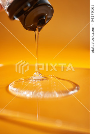 A drop of body gel or shampoo pouring from above on a yellow saturated background. A drop of body gel or shampoo pouring from above on a yellow saturated background. 94179162