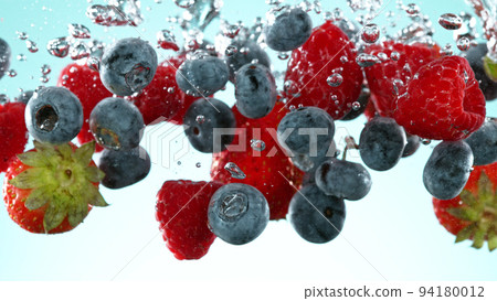 Berries fruit pieces falling underwater on blue background. 94180012