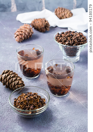 Infusion of pine nut shells in glasses and pine nuts on the table. Alternative medicine. Vertical view Infusion of pine nut shells in glasses and pine nuts on the table. Alternative medicine. Vertical view 94180179