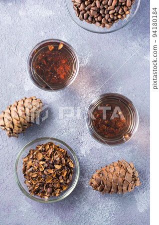 Decoction of pine nut shells in glasses and pine nuts on the table. Alternative medicine. Vertical and top view Decoction of pine nut shells in glasses and pine nuts on the table. Alternative medicine. Vertical and top view 94180184
