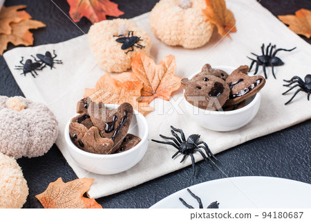 A delicious Halloween treat - gingerbread cookies with chocolate icing in bowls on a table with pumpkins and leaves. Traditional celebration, sweet food. A delicious Halloween treat - gingerbread cookies with chocolate icing in bowls on a table with pumpkins and leaves. Traditional celebration, sweet food. 94180687