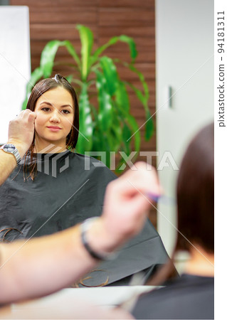 Reflection in the mirror of the young caucasian woman sitting and receiving haircut by male hairdresser at hairdresser salon 94181311