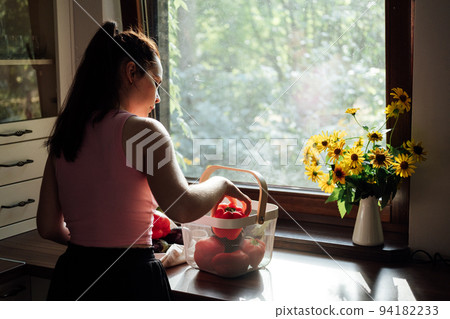 Vegan food and health. Vegans Eat. Young Latina woman holding red Bell pepper near vegetables on table in home kitchen. Vegan food and health. Vegans Eat. Young Latina woman holding red Bell pepper near vegetables on table in home kitchen. 94182233