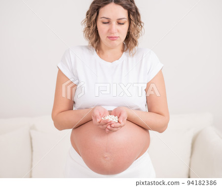 A pregnant woman is holding a handful of white pills. 94182386