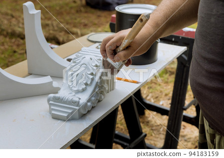 Worker is painting wooden corbels for a kitchen island with a paintbrush 94183159