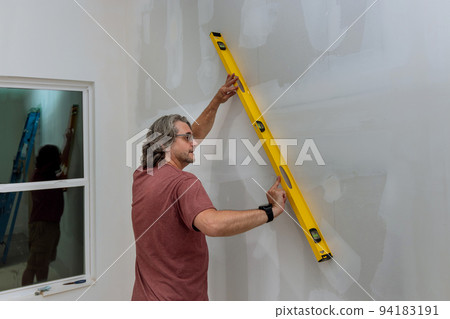 An employee checks the level of a wall of drywall before painting by using a level to make sure the walls are equal 94183191
