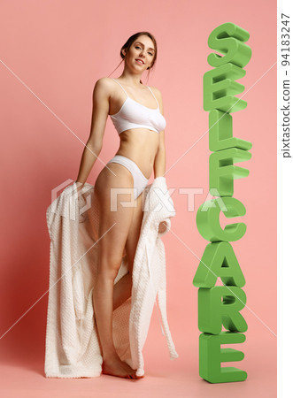 Portrait of slim, beautiful girl in white underwear and dressing gown standing near 3D word of self care over pink background Portrait of slim, beautiful girl in white underwear and dressing gown standing near 3D word of self care over pink background 94183247