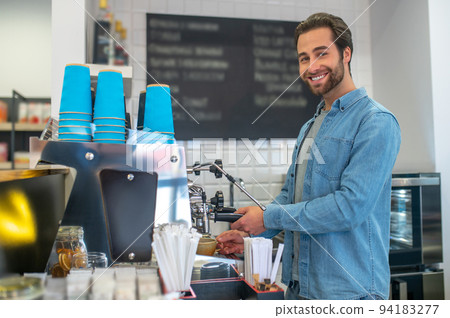 Barista making coffee in the cafe and looking contented Barista making coffee in the cafe and looking contented 94183277