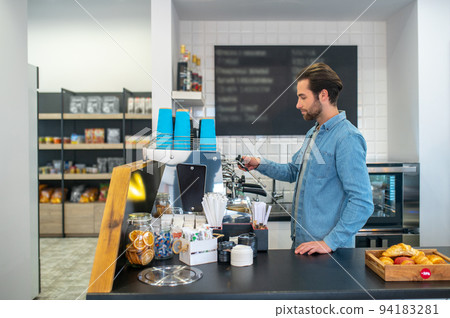 Barista making coffee in the cafe and looking contented Barista making coffee in the cafe and looking contented 94183281