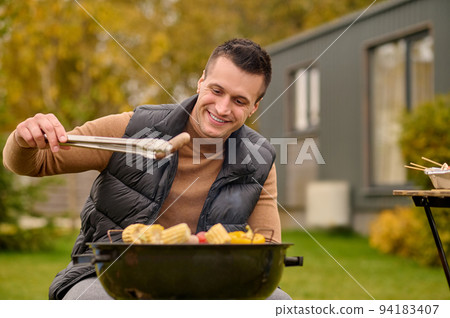 Joyous man cooking food in the backyard Joyous man cooking food in the backyard 94183407