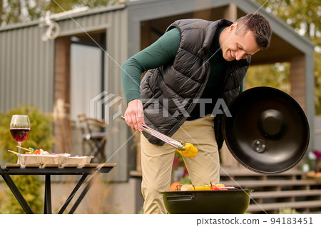 Joyful cook flipping sliced vegetables on the grill 94183451