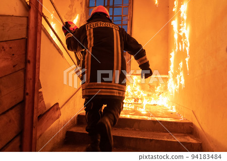 Brave Fireman going upstairs to save and rescue people in a Burning Building. Open fire and flame. Brave Fireman going upstairs to save and rescue people in a Burning Building. Open fire and flame. 94183484