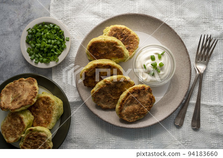 Zucchini fritters, stack of vegetarian zucchini pancakes in a plate, with fresh herbs and sour cream. Zucchini fritters, stack of vegetarian zucchini pancakes in a plate, with fresh herbs and sour cream. 94183660