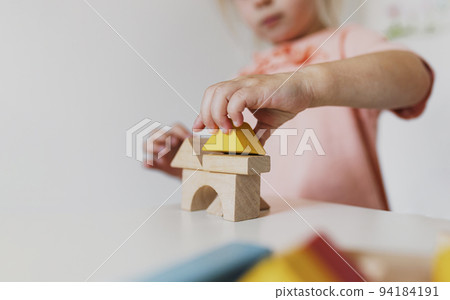 Little child girl playing wooden building blocks at home or kindergarten. Development and construction concept. Multi-colored educational bricks for early learning and education for young children. Little child girl playing wooden building blocks at home or kindergarten. Development and construction concept. Multi-colored educational bricks for early learning and education for young children. 94184191