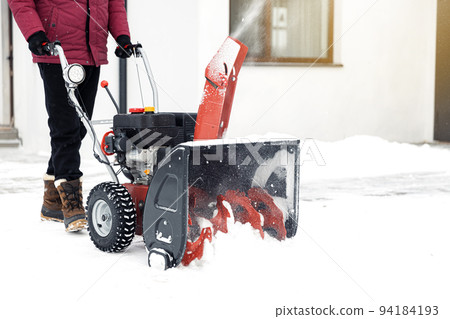Closeup of red snow blower in action. Senior mature man outdoor in front of house using snowblower machine for removing snow on yard. Snow thrower in winter outside home. Young worker guy blowing snow 94184193