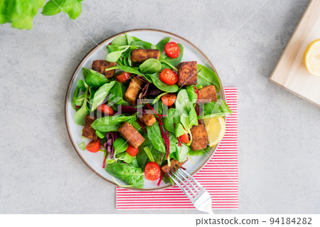 Top view healthy salad with roasted tempeh, cherry tomato, beetroot straws, spinash and lettuce leaves on plate. Tempeh is fermented soy bean. Plant based protein. Healthy Cooking and eating. Go vegan Top view healthy salad with roasted tempeh, cherry tomato, beetroot straws, spinash and lettuce leaves on plate. Tempeh is fermented soy bean. Plant based protein. Healthy Cooking and eating. Go vegan 94184282