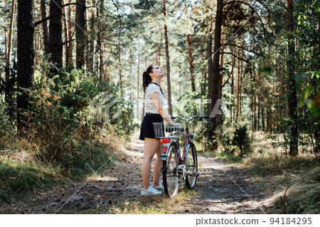 Bicycle Tourism. Road Biking Trails. Bicycles for rent. Single woman riding bike in pine forest in sunny day Bicycle Tourism. Road Biking Trails. Bicycles for rent. Single woman riding bike in pine forest in sunny day 94184295