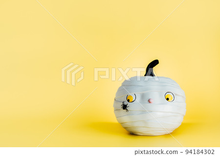 Funny and cute pumpkin mummy with spider on the yellow background. White Pumpkin with scaried and worried look. Fear of insects. Halloween decor and background with copy space. Selective focus Funny and cute pumpkin mummy with spider on the yellow background. White Pumpkin with scaried and worried look. Fear of insects. Halloween decor and background with copy space. Selective focus 94184302
