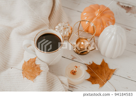 Details of Still life, cup of tea or coffee, pumpkins, candle, brunch with leaves on white table background, home decor in a cozy house. Autumn weekend concept. Fallen leaves and home decoration. 94184583