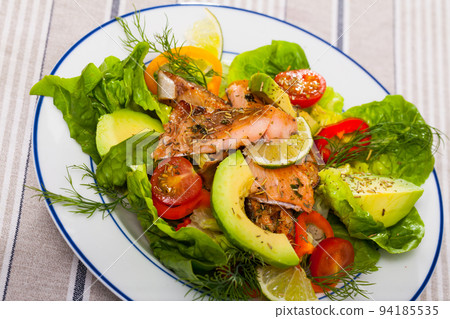 Delicious salad of fried trout, avocado, tomatoes and herbs at plate 94185535