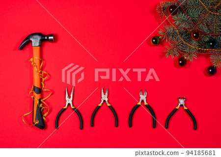 Construction inturments hammer, pliers, cutters, round-cutters and tongs with a Christmas fir branch on a red background. Banner for construction store and repair. New Year 94185681