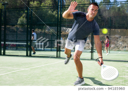 Male players playing padel in a padel court outdoor behind net 94185960