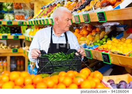 Male supermarket worker carries box of green chili peppers Male supermarket worker carries box of green chili peppers 94186004