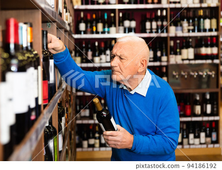 Attentive pensioner chooses red wine in a liquor store Attentive pensioner chooses red wine in a liquor store 94186192