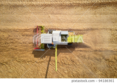 Harvest season, Aerial view of harvesting combine working in agricultural field Harvest season, Aerial view of harvesting combine working in agricultural field 94186361