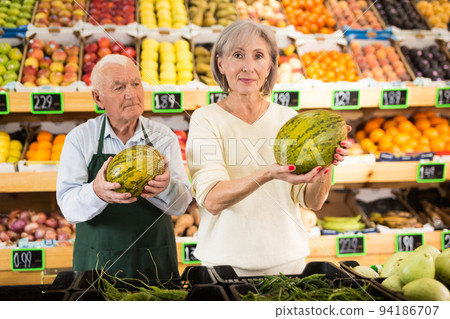 Grocery supermarket worker helping woman pick watermelon 94186707