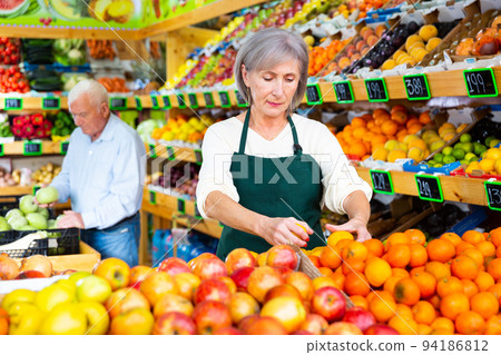 Female supermarket worker stacking fruits on shelf in sales room Female supermarket worker stacking fruits on shelf in sales room 94186812
