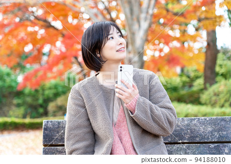 A young woman using a smartphone in a park with autumn leaves 94188010