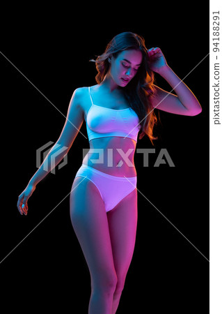 Portrait of young gorgeous woman in white cotton underwear isolated over dark background in neon light. Wellness, fitness, diet, beauty of female body 94188291