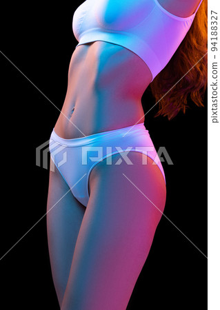 Cropped image of sportive female body in white cotton underwear isolated over dark background in neon light. Concept of beauty, fitness, health, spa Cropped image of sportive female body in white cotton underwear isolated over dark background in neon light. Concept of beauty, fitness, health, spa 94188327