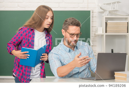 curious kid and dad sitting in classroom with copybook and computer at blackboard, communication curious kid and dad sitting in classroom with copybook and computer at blackboard, communication 94189206