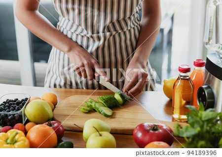 Close up on housewife woman, girl hands slicing cucumber at kitchen on chopping board. Female making healthy low calories salad, prepare green detox shake or smoothie for dieting eating at home. 94189396