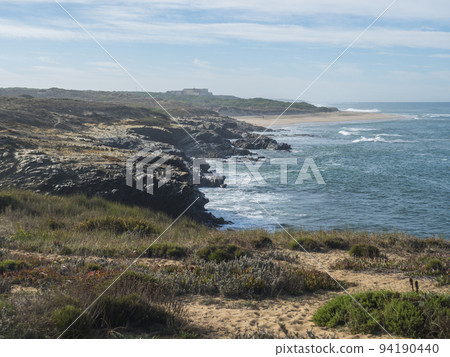 View of empty Praia do Sissal sand beach with ocean waves and sharp rock and cllifs at wild Rota Vicentina coast near Porto Covo, Portugal. 94190440