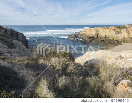 View of empty Praia Selvagem sand beach with ocean waves and sharp rock and cllifs at wild Rota Vicentina coast near Porto Covo, Portugal. 94190443