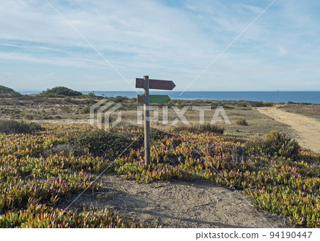 Signpost pointing the way on Praia do Sissal with the colours of Rota Vicentina Route and Fishermans trail beautiful hiking route that mixes sandy beaches, cliffs and vegetation. Porto Covo, Portugal 94190447