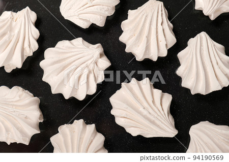 White meringues on a black background, sweet pastries, a dessert of sugar and egg white. White meringues on a black background, sweet pastries, a dessert of sugar and egg white. 94190569