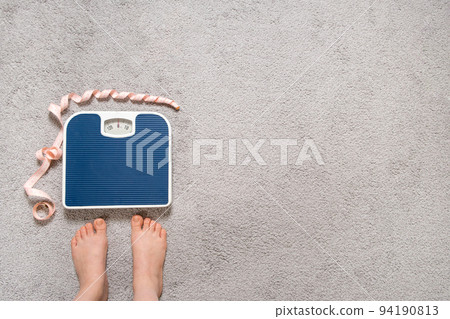 Bare feet and a floor blue scale with a measuring centimeter tape, the concept of losing weight, place for text, top view. Bare feet and a floor blue scale with a measuring centimeter tape, the concept of losing weight, place for text, top view. 94190813