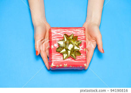 Beautiful red gift box with bow in women's hands, top view, copy space for text. Beautiful red gift box with bow in women's hands, top view, copy space for text. 94190816