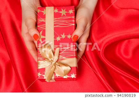 Red beautiful gift with yellow golden bow in the hands of a woman with red nail polish, top view, place for text. Red beautiful gift with yellow golden bow in the hands of a woman with red nail polish, top view, place for text. 94190819
