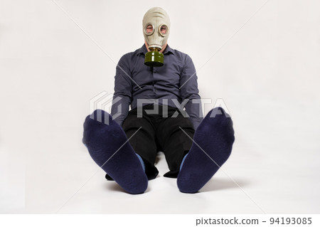 A man in a gas mask sits on a white background, his legs stinking. Unpleasant smell of socks in men. 94193085