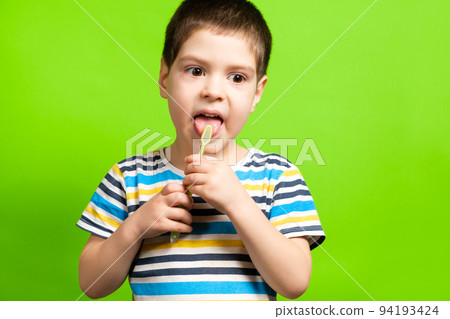 A preschool boy of 4 years cleans with a toothbrush a tongue on a green background. 94193424